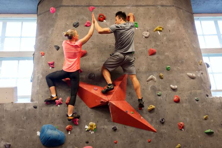 a man and woman on an indoor climbing wall high-fiving each other