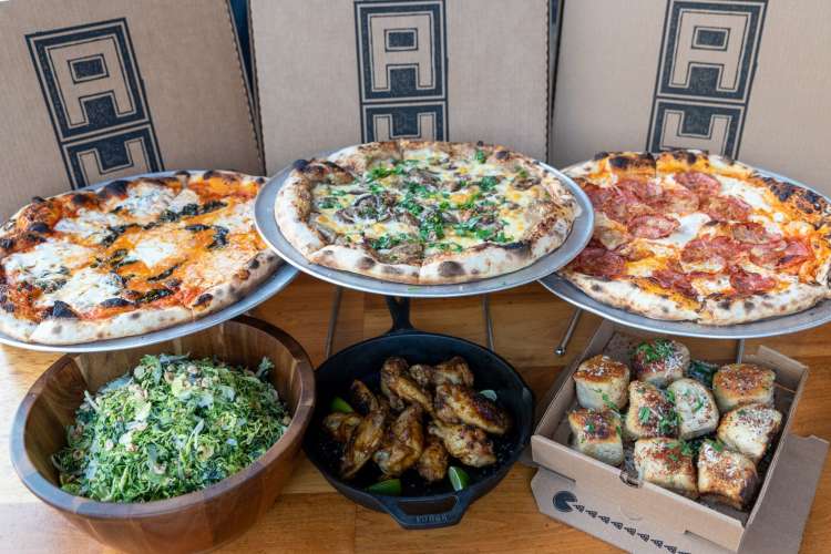 a table full of pizzas, salad and bread from Area Four