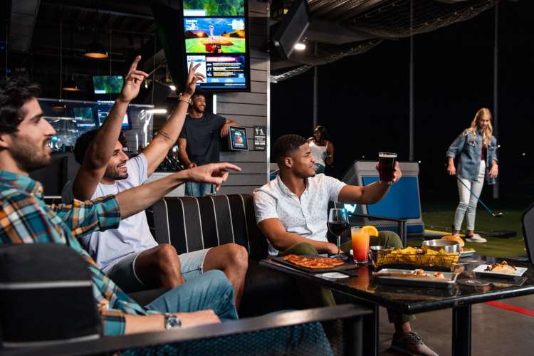 Three men cheer on a friend about to putt at TopGolf.