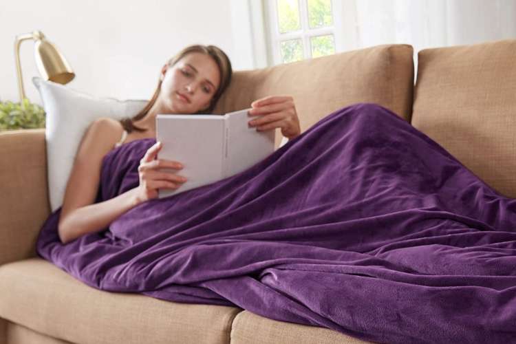 woman lounging on the couch underneath a purple weighted blanket