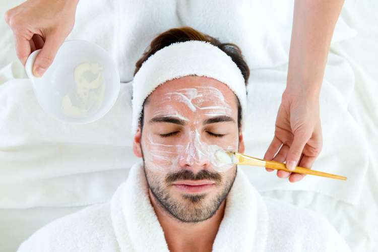 a man in a white robe having a clay mask applied to his face