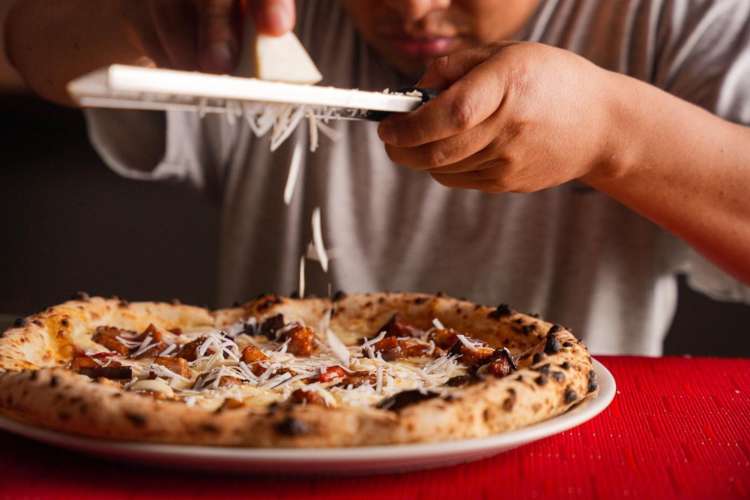 a man grating cheese over a pizza