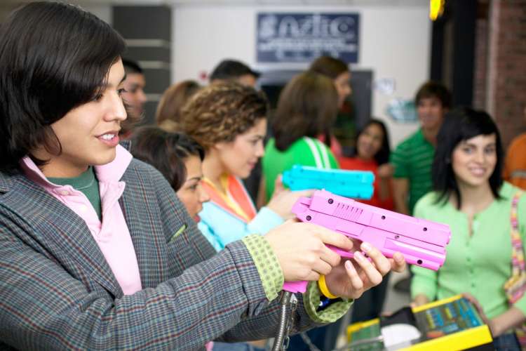 a woman playing an arcade game with a toy gun while friends look on