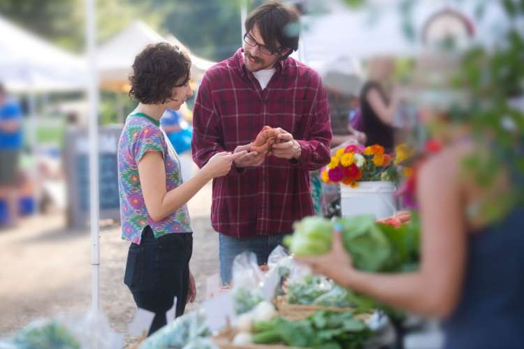 a woman and man examine flowers at a farmers market