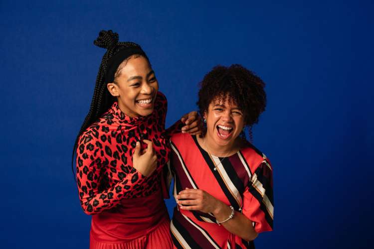 two women laughing together in front of a blue background