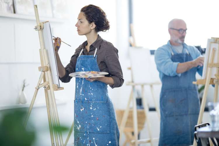 two people in denim aprons painting in a studio