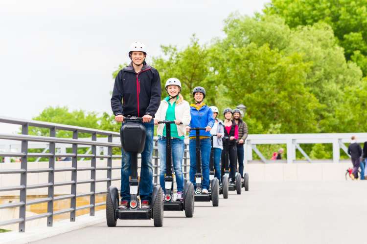 a line of people in helmets ride segways beside a bridge