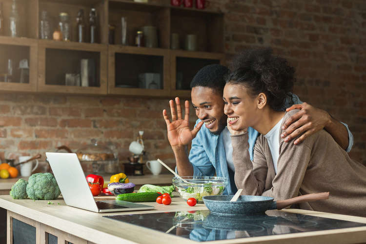 young couple waving at the laptop during virtual dinner party