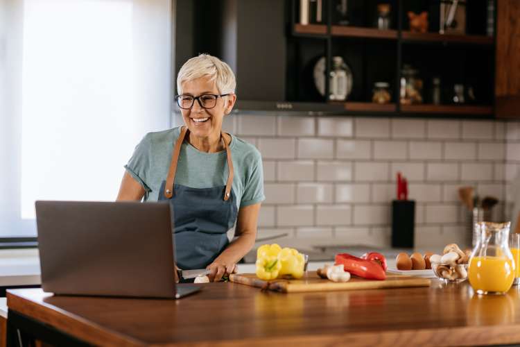 a woman sits at her laptop enjoying an online cooking class