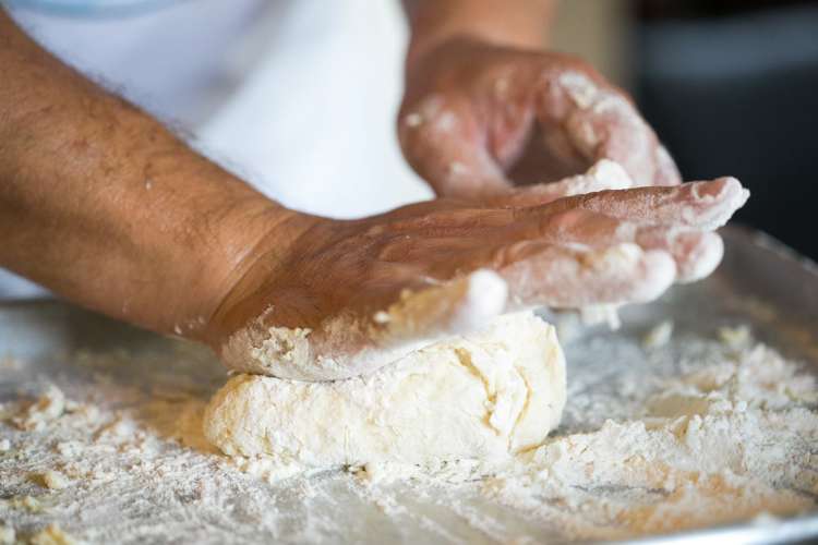 chef kneading deep dish pizza dough on a floured work surface