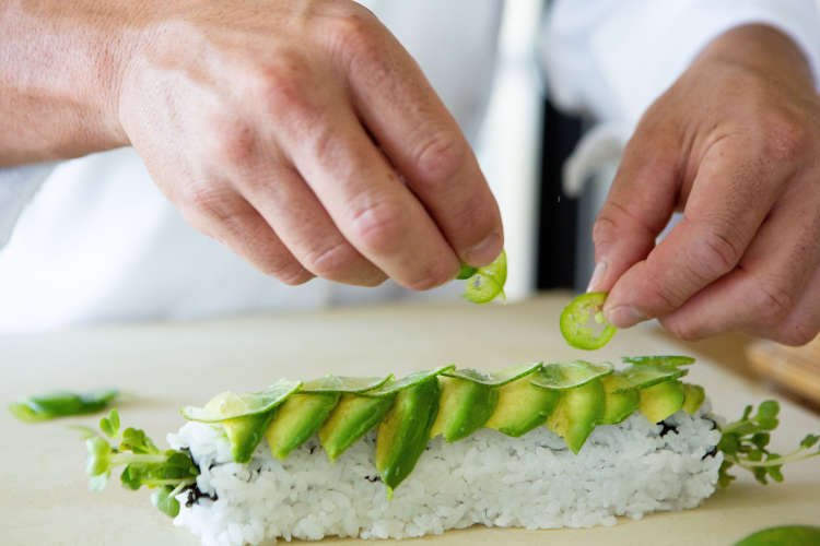 chef preparing a sushi roll with slices of avocado and cucumber