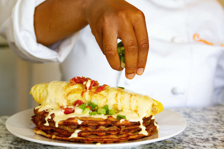A chef's hand dropping spring onions on a plate of food
