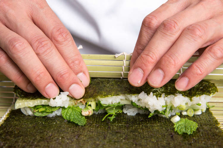 chef rolling sushi with a bamboo mat