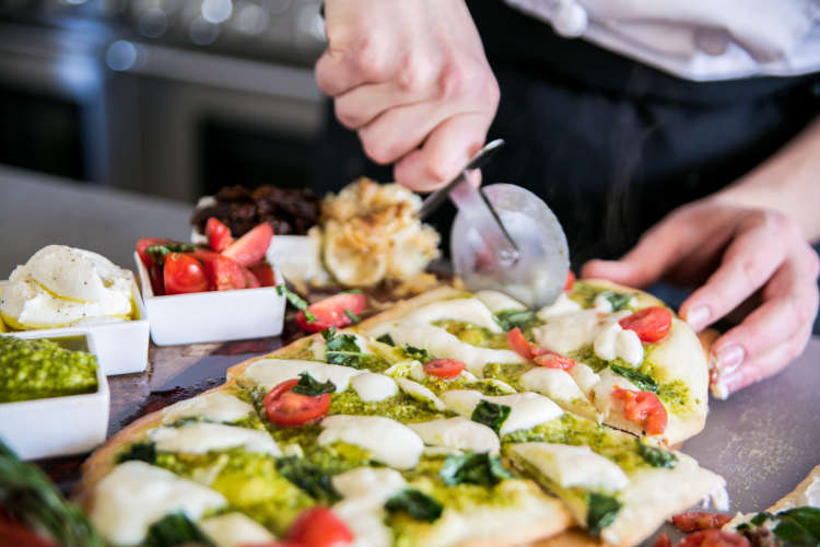 chef rolling a pizza cutter through a flatbread during a cooking class