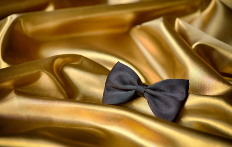 A black bow tie on gold fabric, which is the décor needed for a black tie 50th birthday party idea