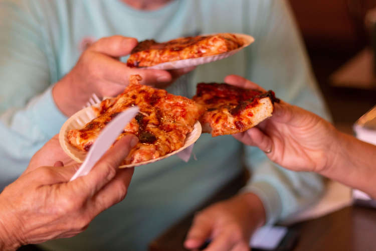 Three hands holding pizza slices on paper plates