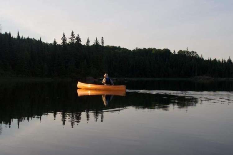 a person in a canoe out on the water at sunset