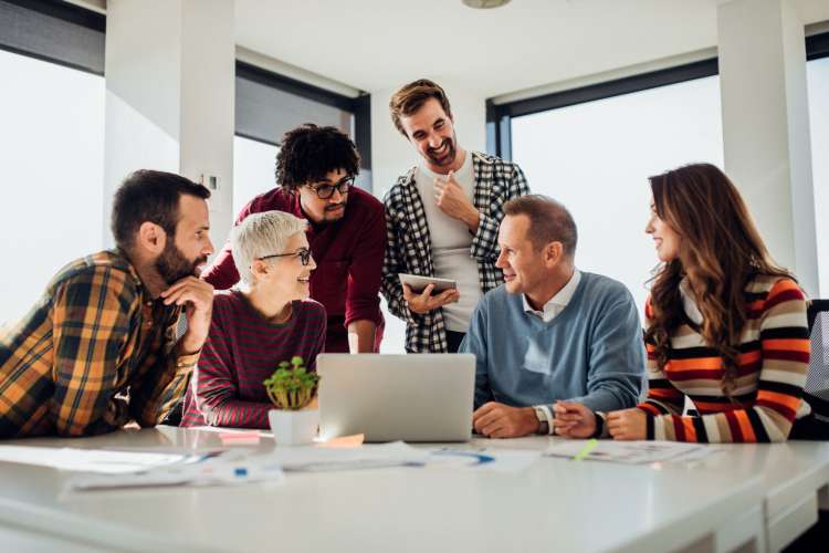 a group of co-workers gathered around a laptop