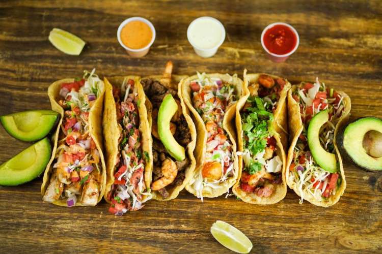 a variety of seafood tacos laid in a row