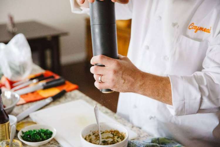 a chef in a Cozymeal apron seasoning ingredients