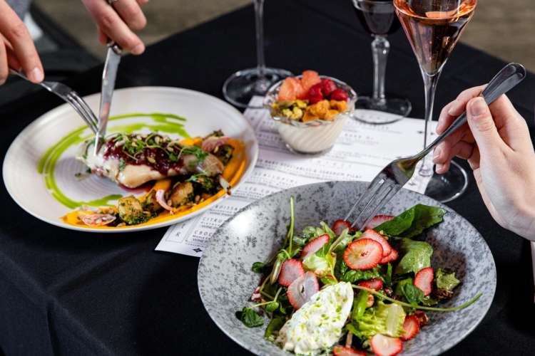 two diners eating a salad and fish and enjoying wine