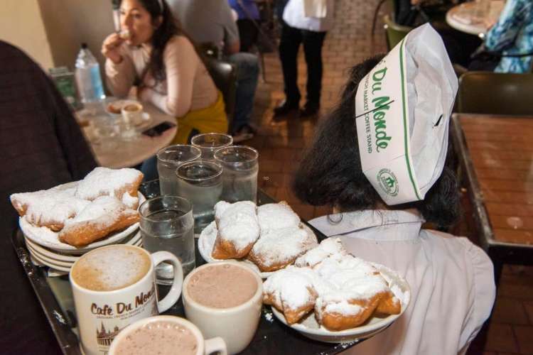 a server carrying a tray of beignets and cafe au lait