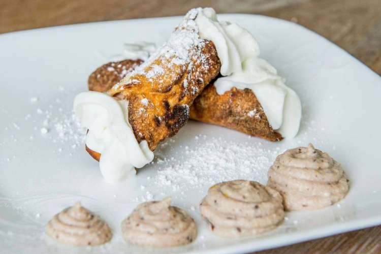 two cannoli with powdered sugar and chocolate drizzled on top