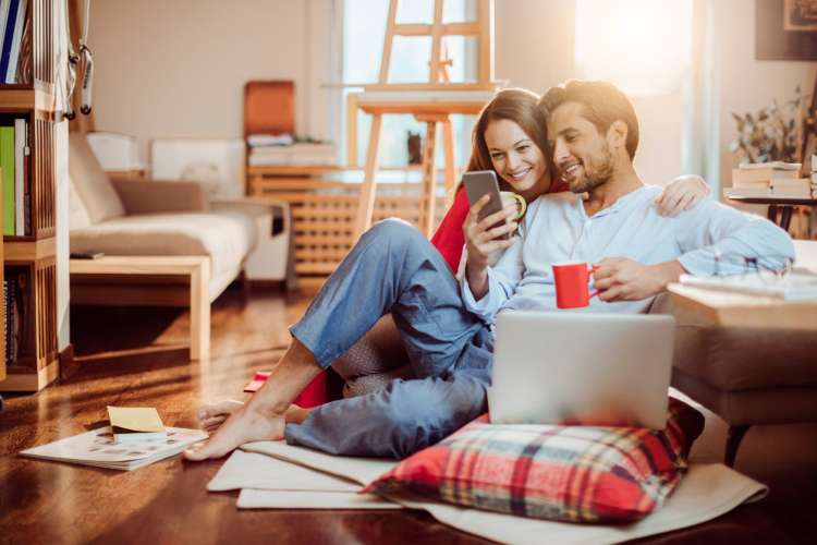 a couple sitting on the floor looking at a smartphone and smiling happily