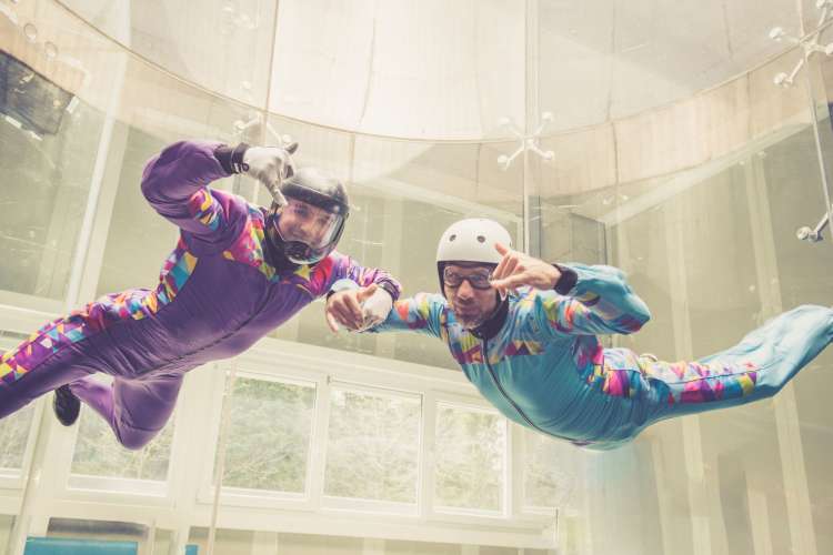 two men indoor skydiving giving the camera a thumbs up