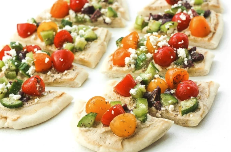 greek salad hummus flatbread is topped with fresh vegetable and savory feta cheese