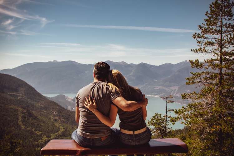 young couple sitting on a bench looking out at the scenery