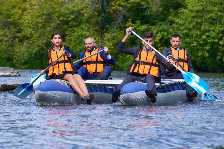 four people in orange life jackets in rafts on a river