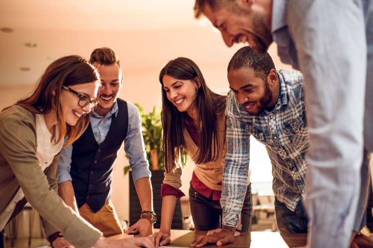 five professionals gather around a sheet and smile