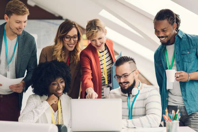 a diverse group of associates look at laptop screen together and smile