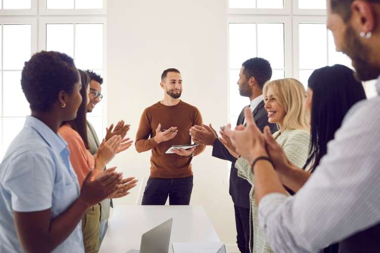 A group of diverse professionals applaud and stand around a table.