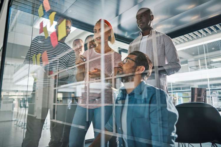 diverse co-workers stick notes to a glass for brainstorming