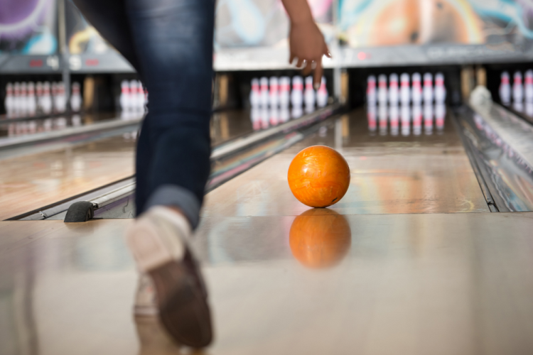 person rolling an orange bowling ball down a bowling lane