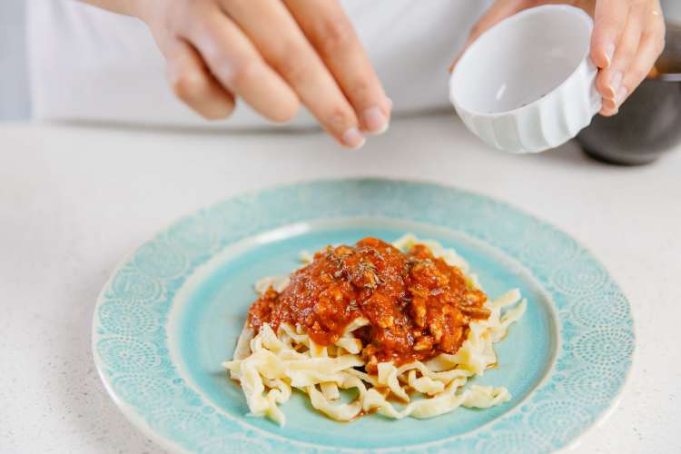 woman garnishing herbs on a pasta dish with tomato sauce