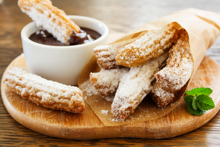 A bag of churros and two separate ones next to a bowl of chocolate sauce