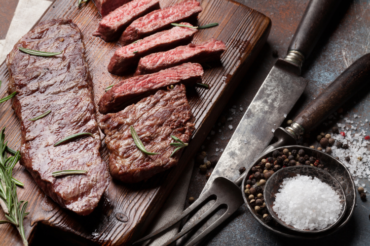 sliced denver steak on a cutting board with cutlery