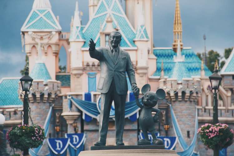 walt disney and mickey mouse statue in front of magic kingdom castle in disney land