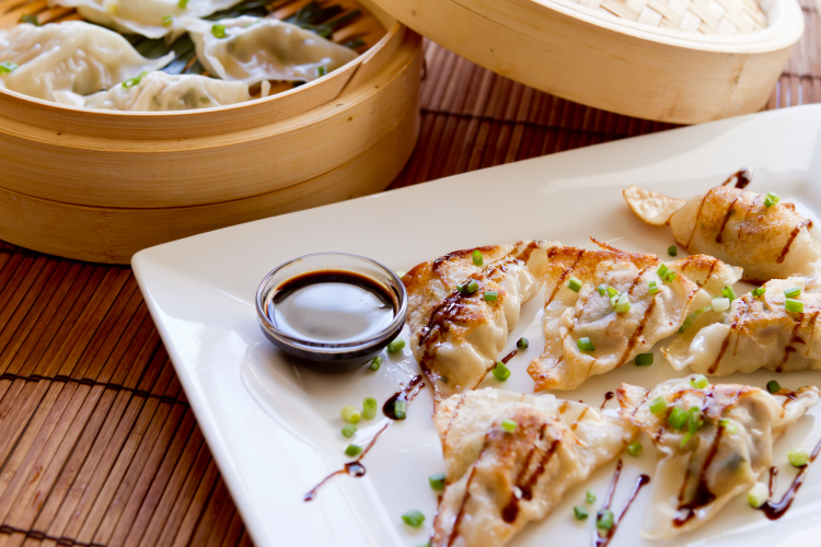 potstickers on a plate and in a bamboo steamer with dipping sauce