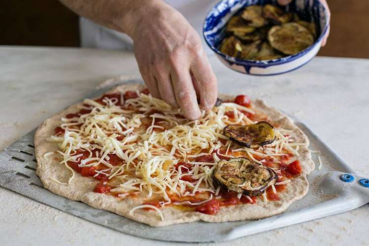 man putting cheese and eggplant slices on a pizza