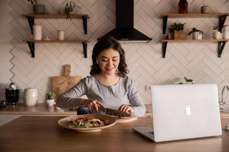 woman chopping vegetables with earbuds in and her laptop