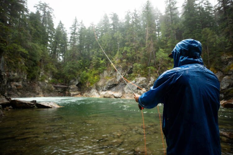 man in a raincoat fly fishing in a wooded stream