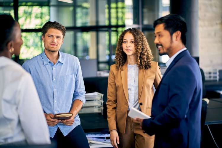 A diverse group of employees stands chatting together at work.