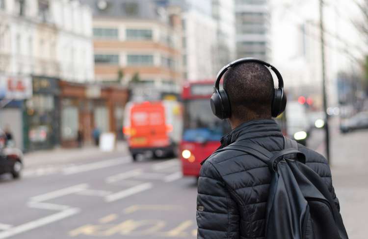 Young man walking down city streets wearing wireless headphones