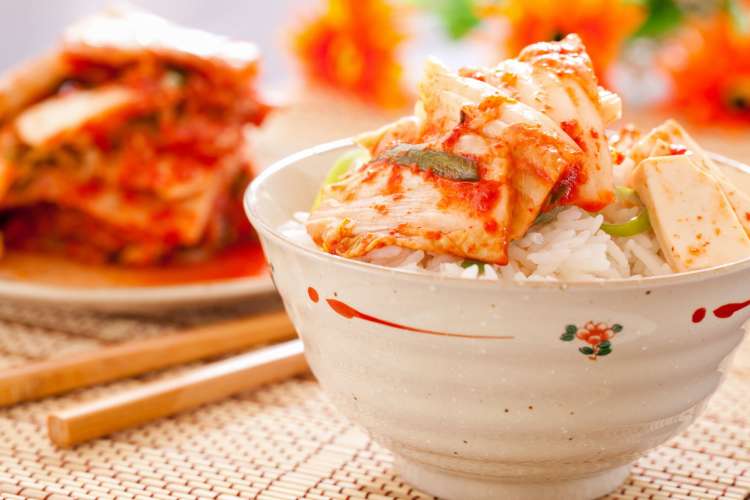 spicy looking kimchi in a bowl of white rice with chopsticks on the table