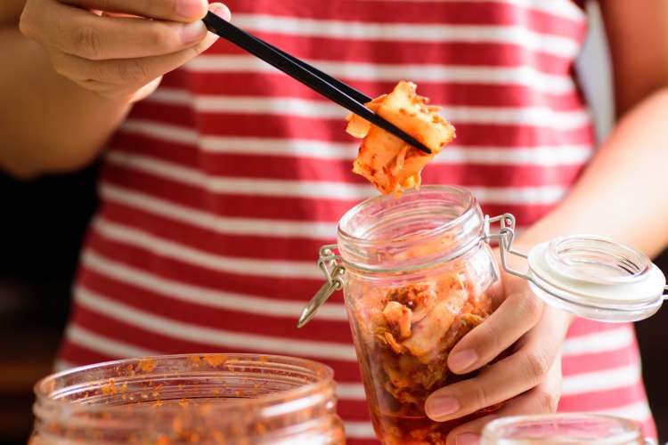 a woman taking kimchi from a small jar with chopsticks