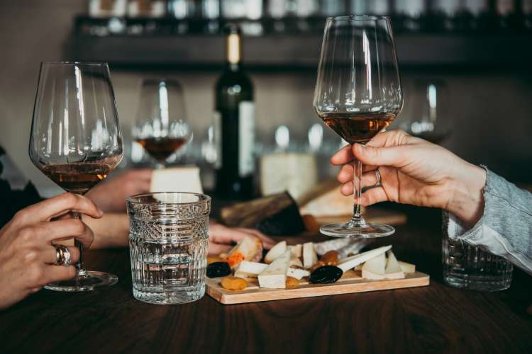 friends holding long-stem wine glasses while enjoying a cheese board